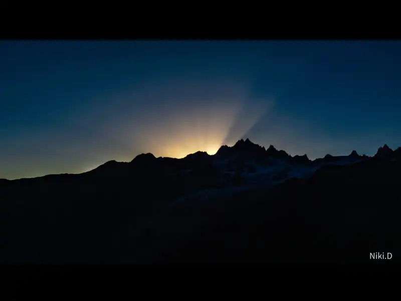 Lever de soleil sur la montagne. On aperçoit quelques rayons dorés perçant le bleu nocturne du ciel.