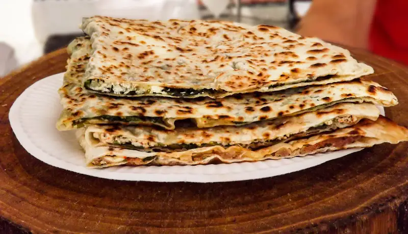 Photos de plats d'un food-truck : Un börek découpé en tranches triangulaire. Il est sur un petit rondin de bois.