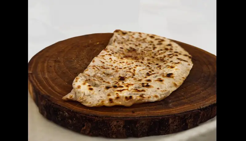 Photo de nourriture : Un borëk, sorte de crêpe croisée avec une pizza, plat d'Anatolie. Il est sur un petit rondin de bois.